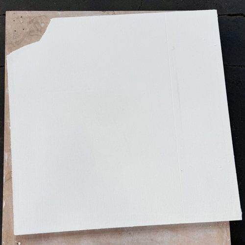 Quadratische, weiße Kalziumsilikatplatte mit kleiner Ecke auf hellem Untergrund