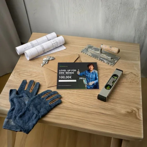 Gutschein mit Bauwerkzeug auf Holztisch, Baupläne und Handschuhe